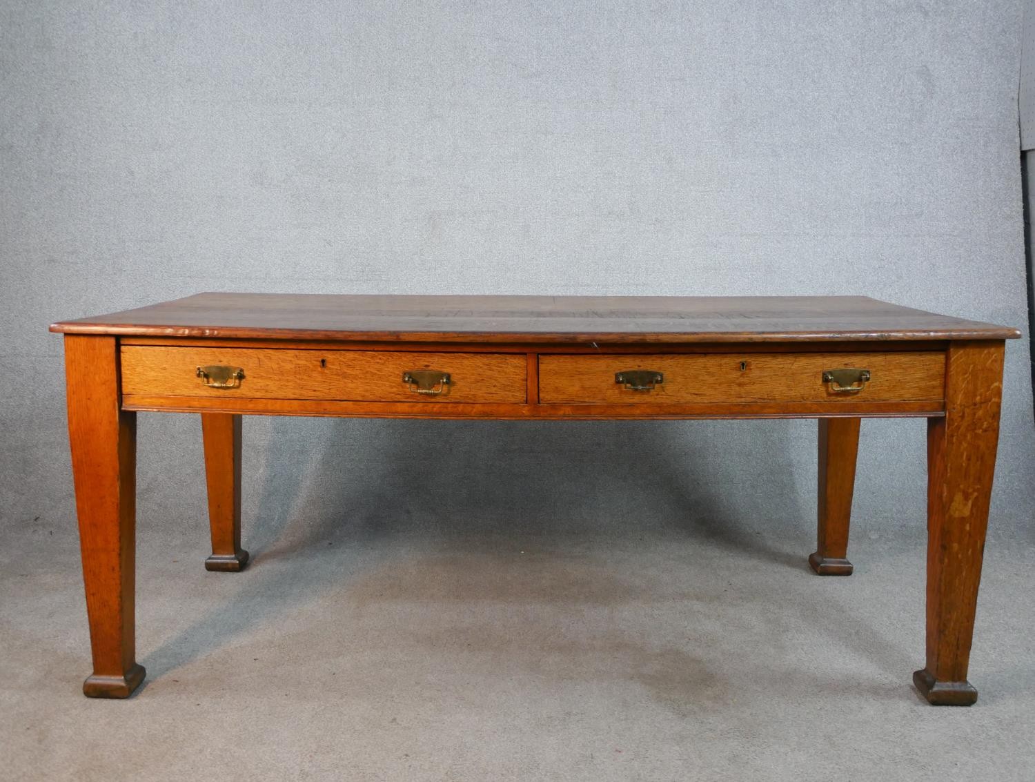 An early 20th century oak two drawer writing table raised on tapering supports terminating in square