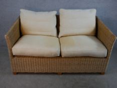 A contemporary two seater wicker conservatory sofa with loose cushions raised on block feet. H.72