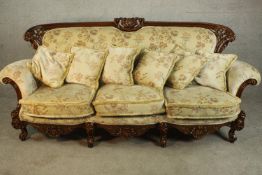 A late 20th century carved and lacquered three seater sofa, upholstered in cream coloured foliate