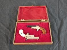 A 20th century cased pair of 22 calibre Butler of America brass short pistols, one with a mahogany