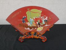 A Chinese red lacquered double sided fan shaped panel, painted with figures in a boat, on a carved