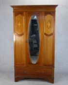 An Edwardian walnut and marquetry inlaid wardrobe, the door with an oval mirror plate, flanked by