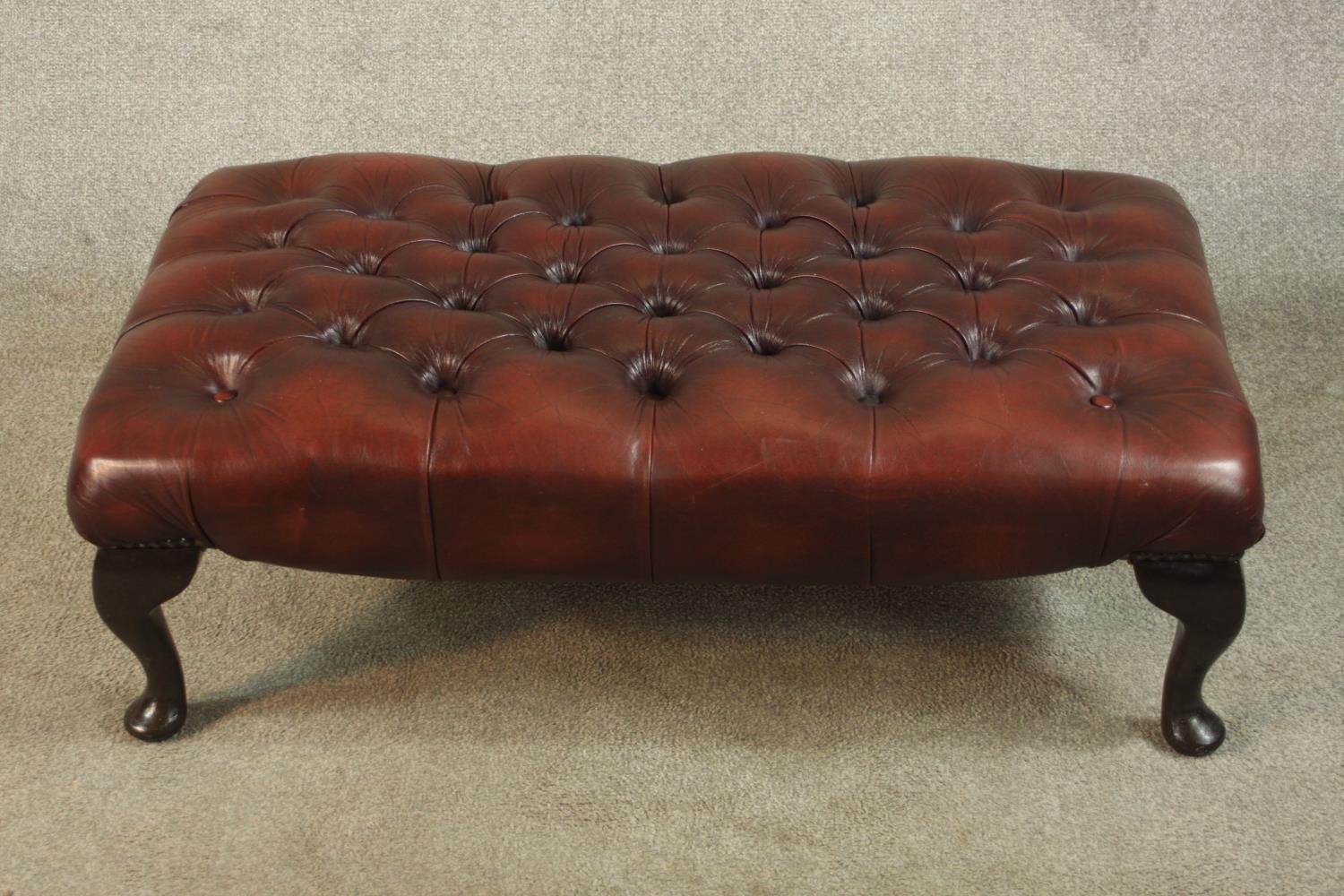 A Georgian style buttoned burgundy leather upholstered stool, of rectangular form, on cabriole legs.