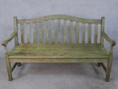 A contemporary teak garden bench, of slatted form, with a curved top rail, the legs joined by