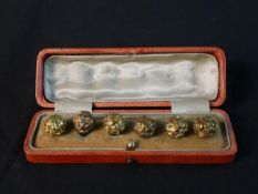 A leather cased set of six 19th century Chinese gilt metal carved floral design robe buttons, one