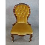 A late Victorian walnut framed spoon back nursing chair raised on cabriole supports terminating in