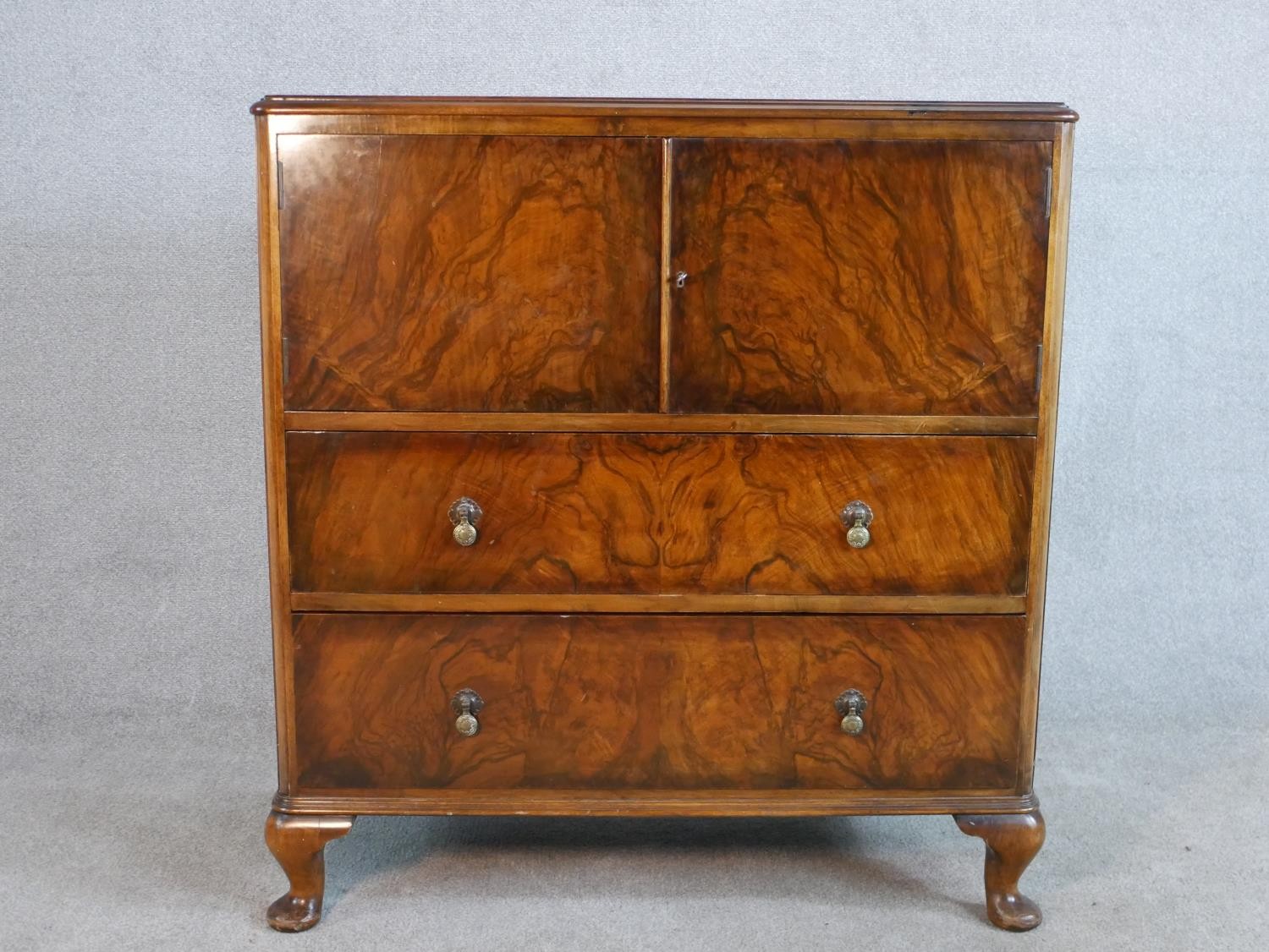 A circa 1930s figured walnut side cabinet, with two cupboard doors enclosing a shelf, over two