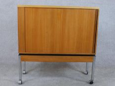A late 20th century teak tambour fronted cabinet, enclosing shelves, on square section tubular