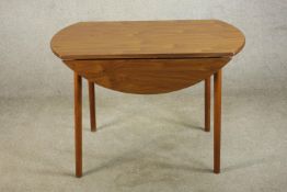 A mid 20th century circular drop leaf table, raised on outswept cylindrical supports, with applied