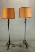 A pair of painted wrought iron standard lamps, each raised on three scroll supports, with orange