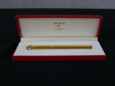 A boxed gold plated Must de Cartier gold plated rollerball pen, with engine turned decoration. H.2