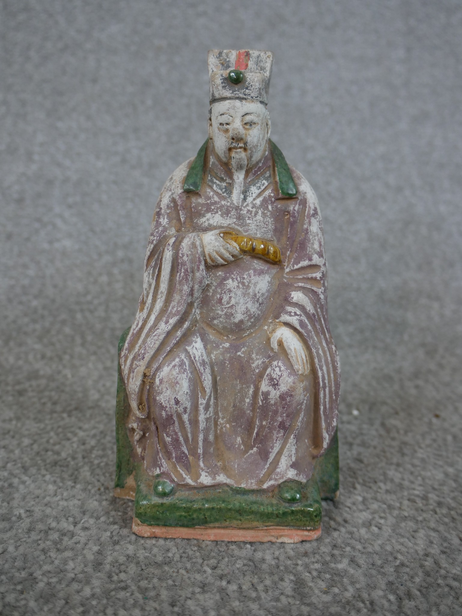 A Chinese painted pottery figure of a seated bearded figure on raised square plinth. H.15 W.26 D.