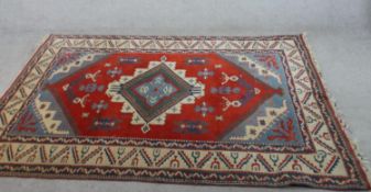 A 20th century Kazak style red ground woollen carpet, with central lozenge within a geometric