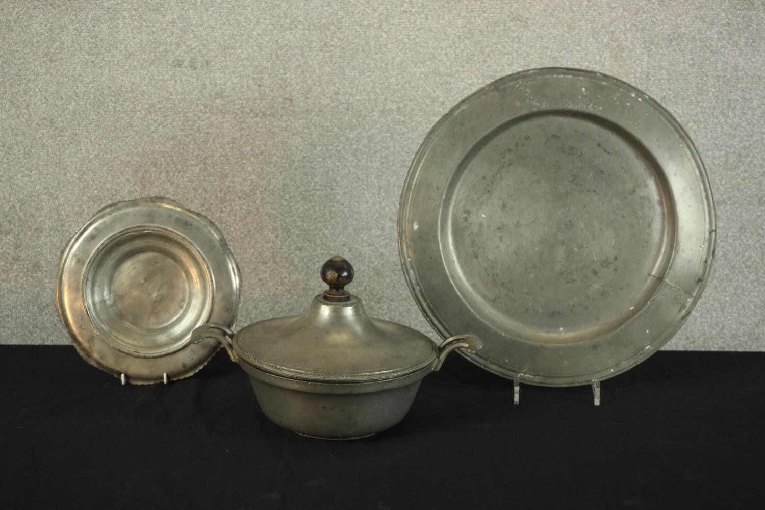 Three pieces of pewter comprising of pewter comprising of two chargers and a twin handled tureen and