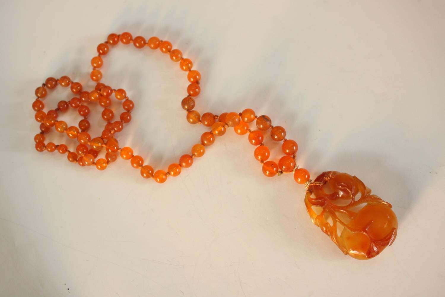 An early 20th century Chinese carved carnelian necklace, the carved pendant in the form of two