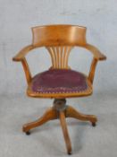 An early 20th century oak framed Captains style open arm desk chair, with rotating seat raised on