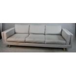 A contemporary three seater Calligaris settee, upholstered in grey fabric raised on shaped beech
