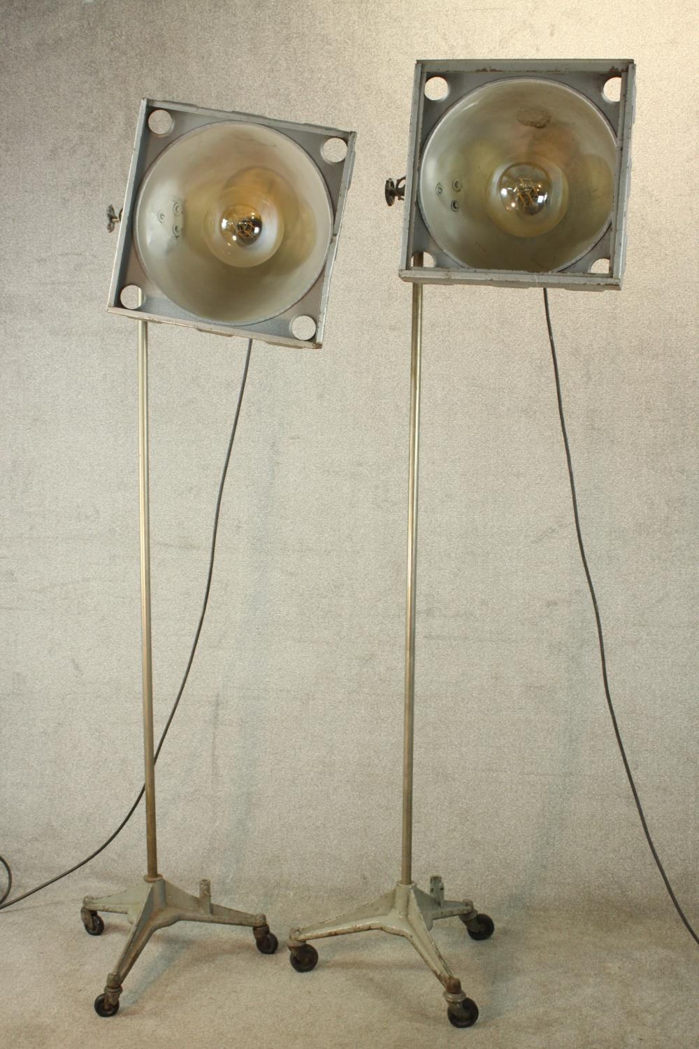 A pair of 20th century pair of industrial floor standing lamps, raised on three splayed supports