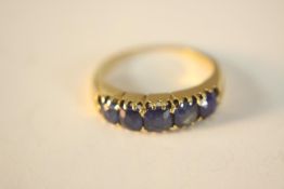A yellow metal (tests higher than 9ct) sapphire carved half hoop ring. Set with five cushion