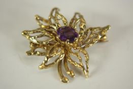 A 9ct yellow gold and amethyst stylized floral brooch. Set to centre with an oval mixed cut amethyst