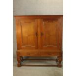 A late 19th century oak two door cupboard with two drawers below, raised on heavily carved