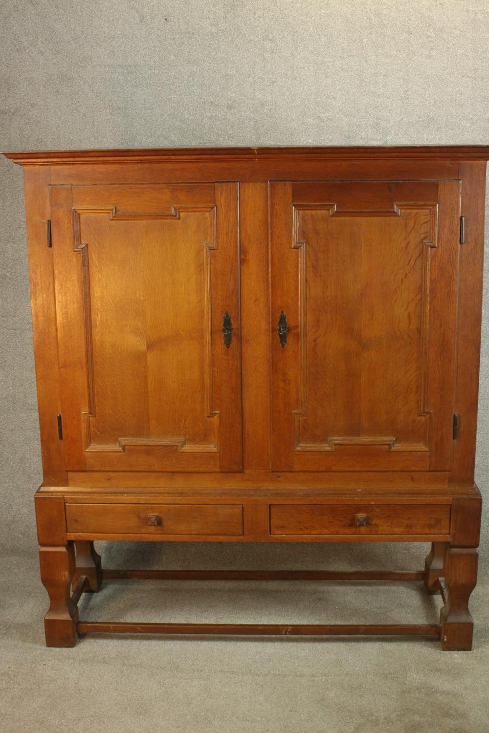 A late 19th century oak two door cupboard with two drawers below, raised on heavily carved