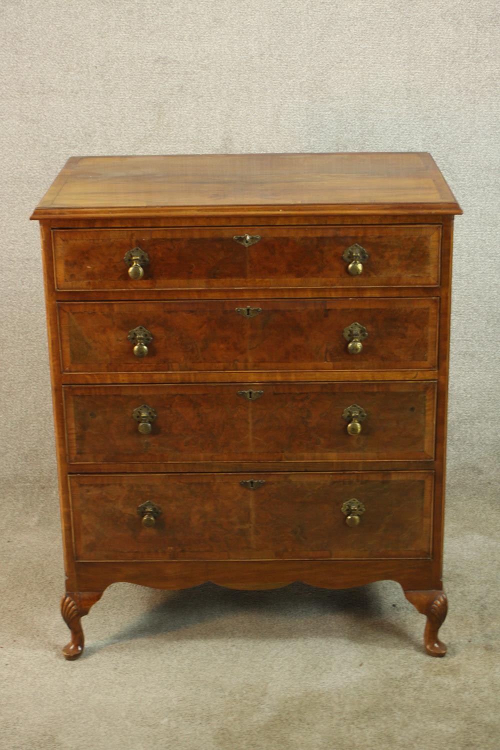 A 20th century walnut veneered chest of four graduating drawers, with brass swing handles, raised on