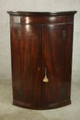 A George III mahogany bow fronted two door corner cabinet, the doors opening to reveal four shelves.