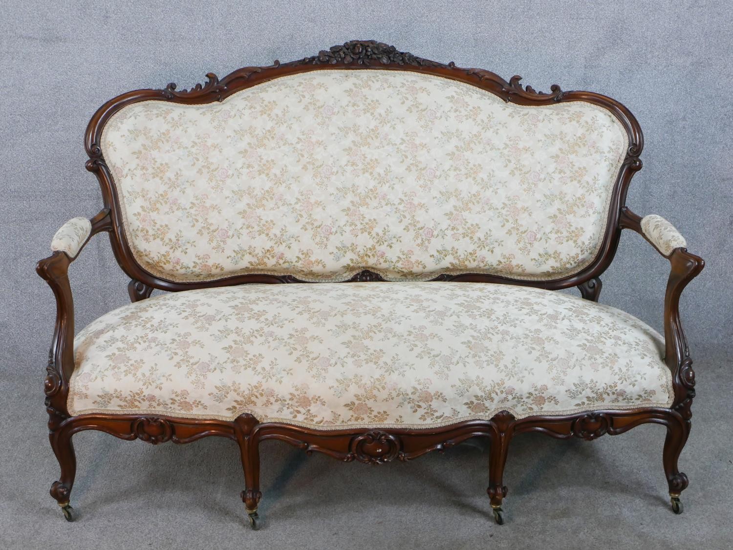 A 20th century French carved mahogany framed open arm settee, upholstered in cream fabric, raised on