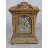 A late 19th/early 20th century carved oak mantle clock, the brass dial with black Arabic numerals,