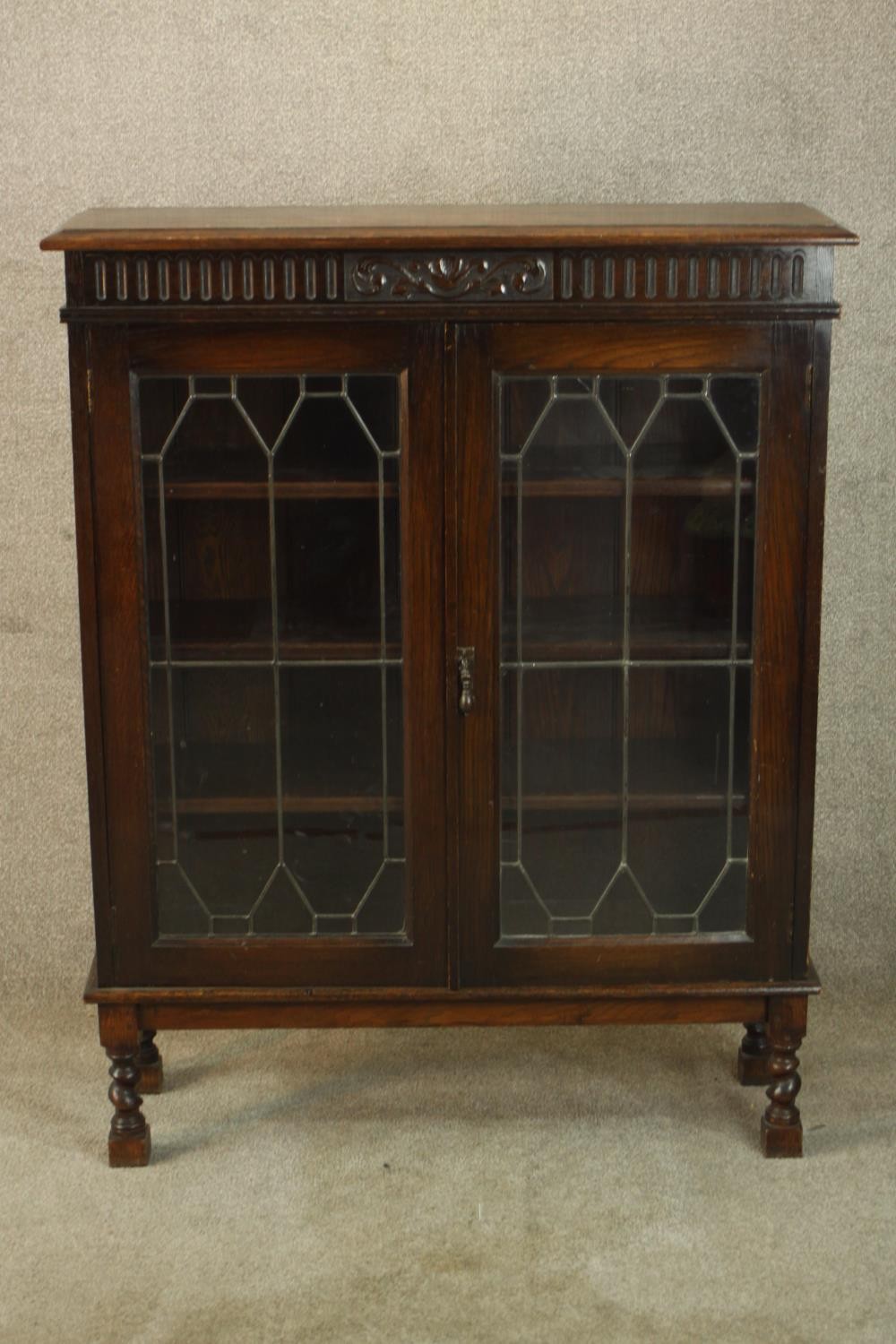 An early 20th century carved oak twin door leaded glass display cabinet, raised on turned supports