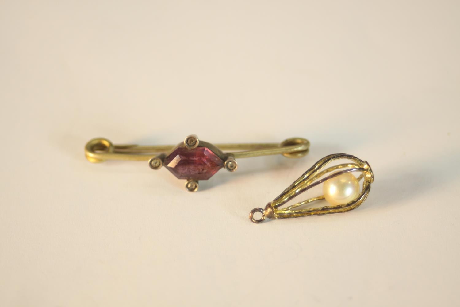 A brass Amethyst paste set bar brooch and fresh water pearl bead in a yellow metal cage. L.4cm (