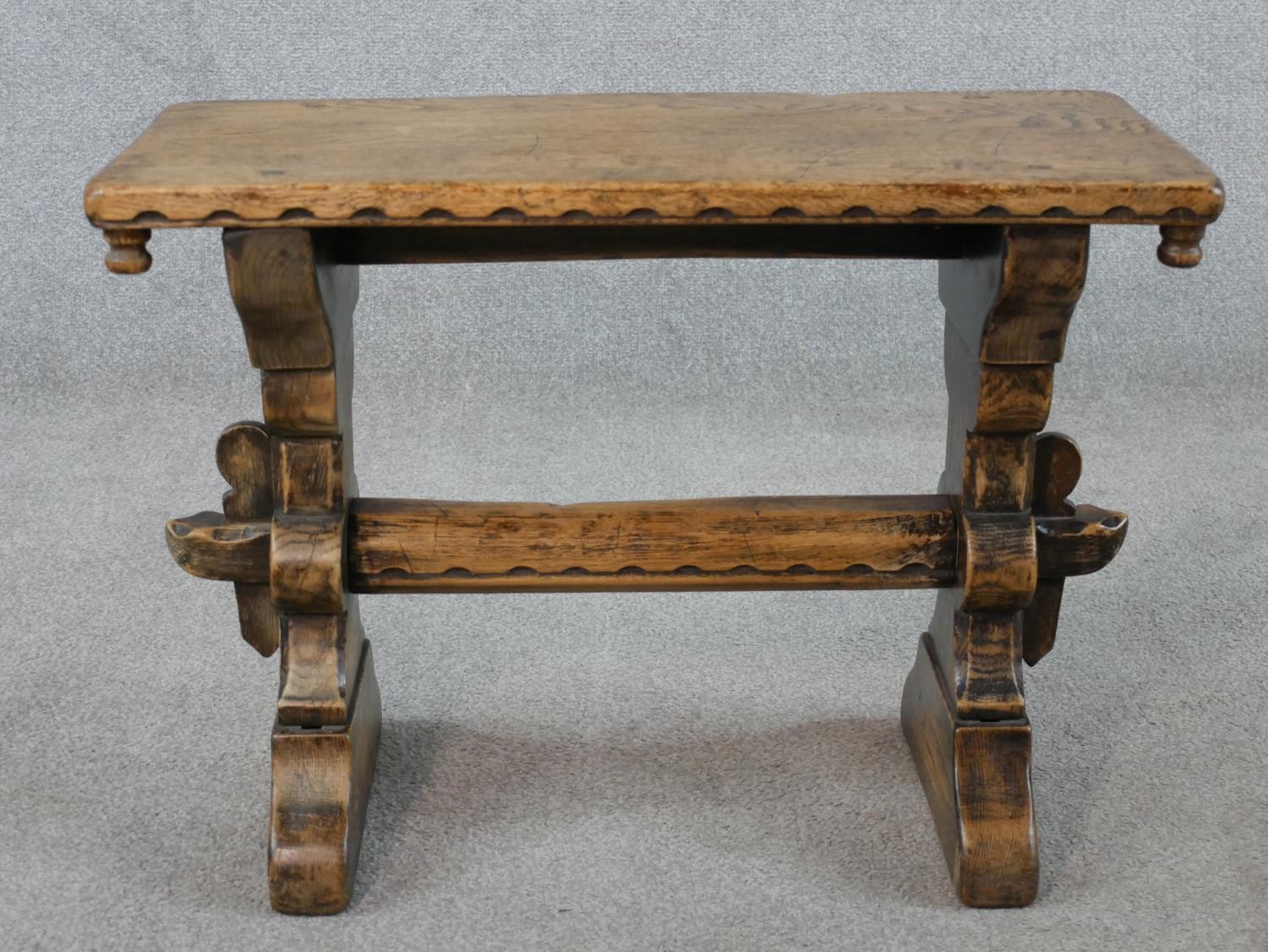 A late 19th/early 20th century stained oak stool, raised on carved trestle supports with block feet.