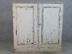 An early 20th century painted pine two door cabinet, opening to reveal four shelves, raised on