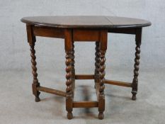 An early 20th century oak drop leaf gate leg table, raised on barley twist supports terminating in