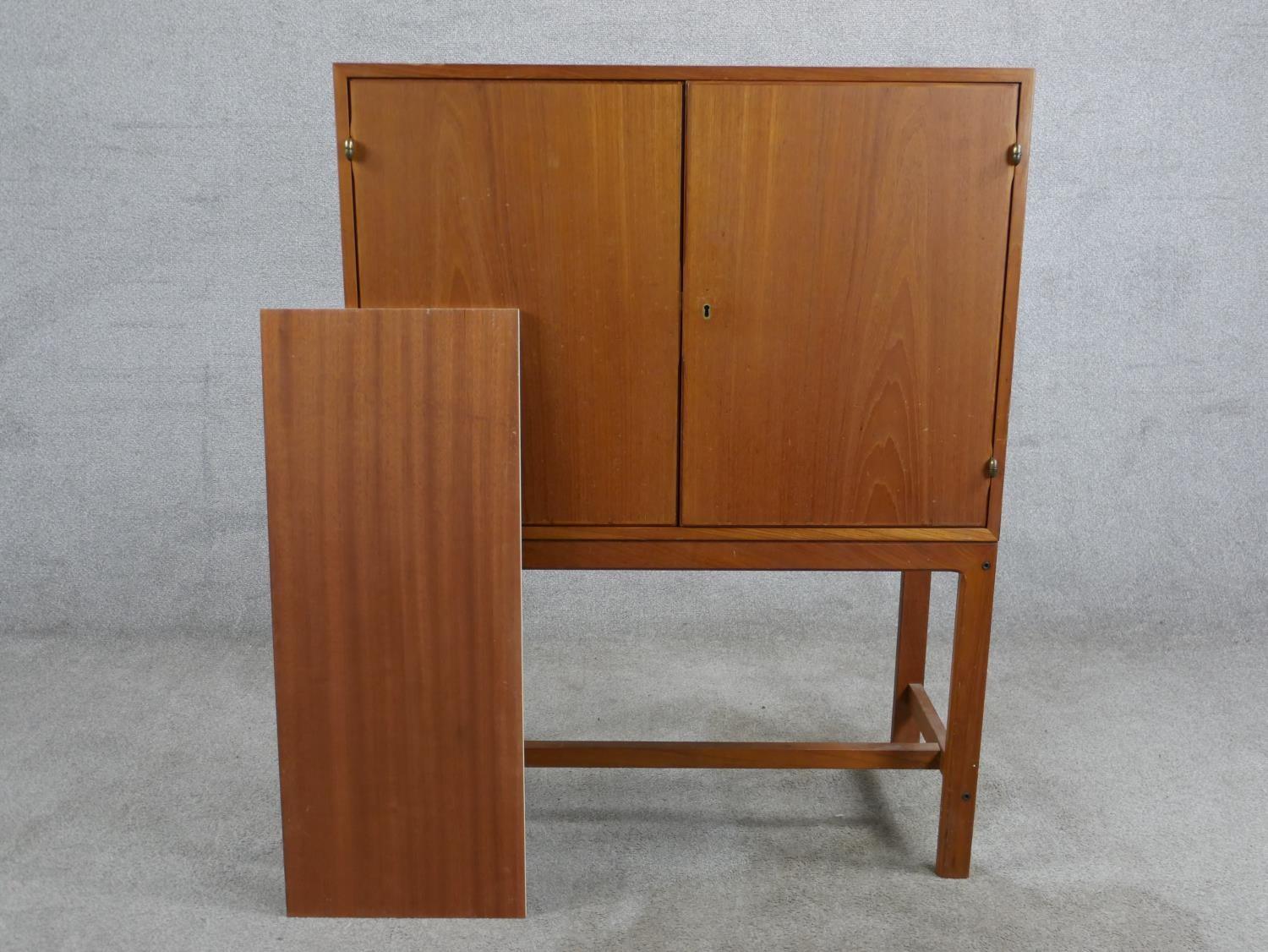A mid 20th century Danish teak two door cupboard, opening to reveal three shelves, raised on