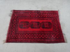 A 20th century red ground woollen rug, with three central lozenges within a geometric border. H.
