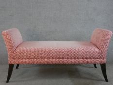 A contemporary mahogany framed long stool upholstered in pink and white fabric, raised on tapering