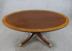 A Regency style inlaid mahogany oval coffee table raised on turned central column on four outswept