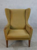 A mid 20th century teak framed upholstered wing back armchair, raised on tapering supports.