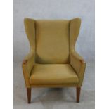 A mid 20th century teak framed upholstered wing back armchair, raised on tapering supports.