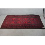 A 20th century red ground Persian woollen rug with four central lozenges within geometric border.