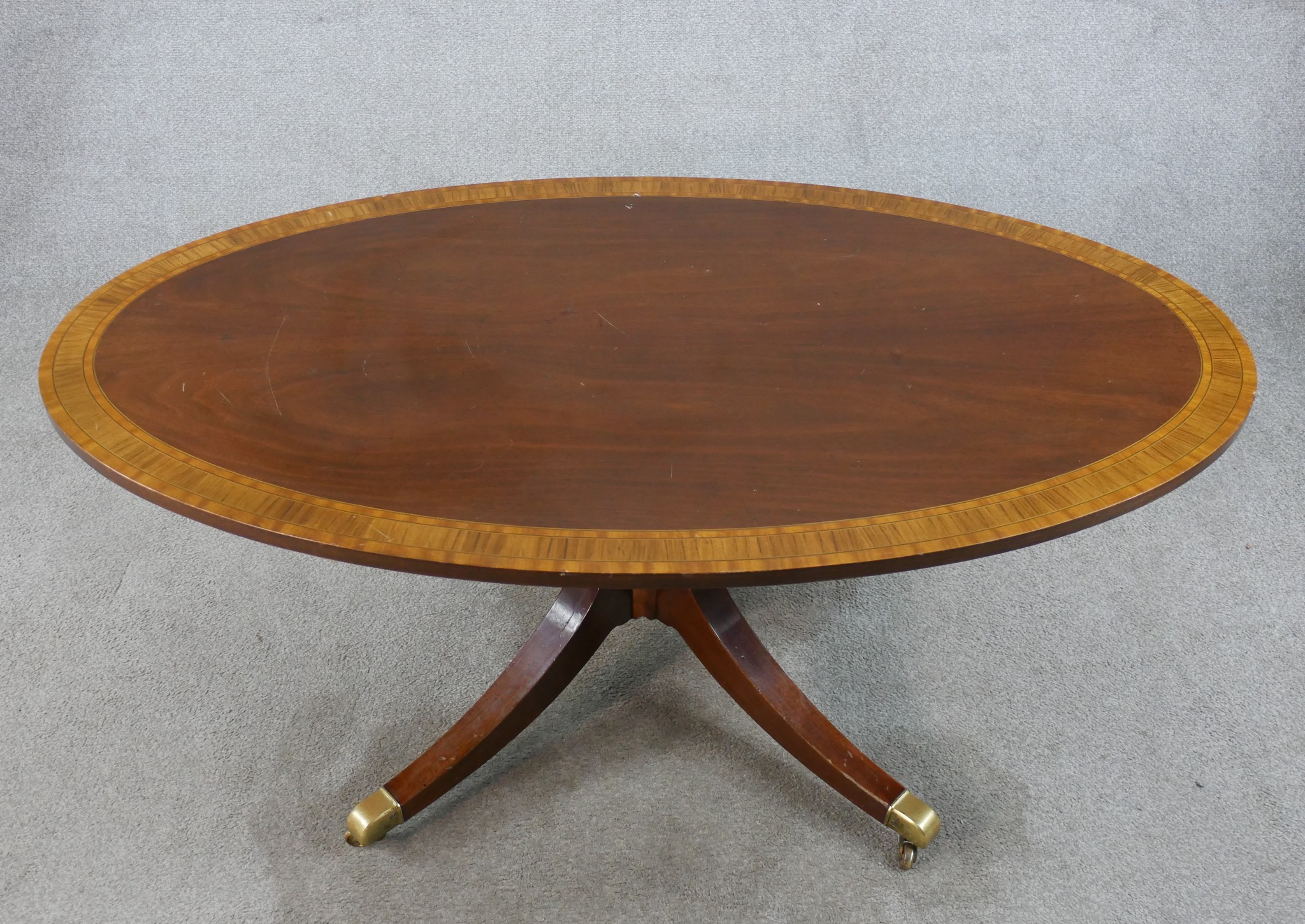 A Regency style inlaid mahogany oval coffee table raised on turned central column on four outswept