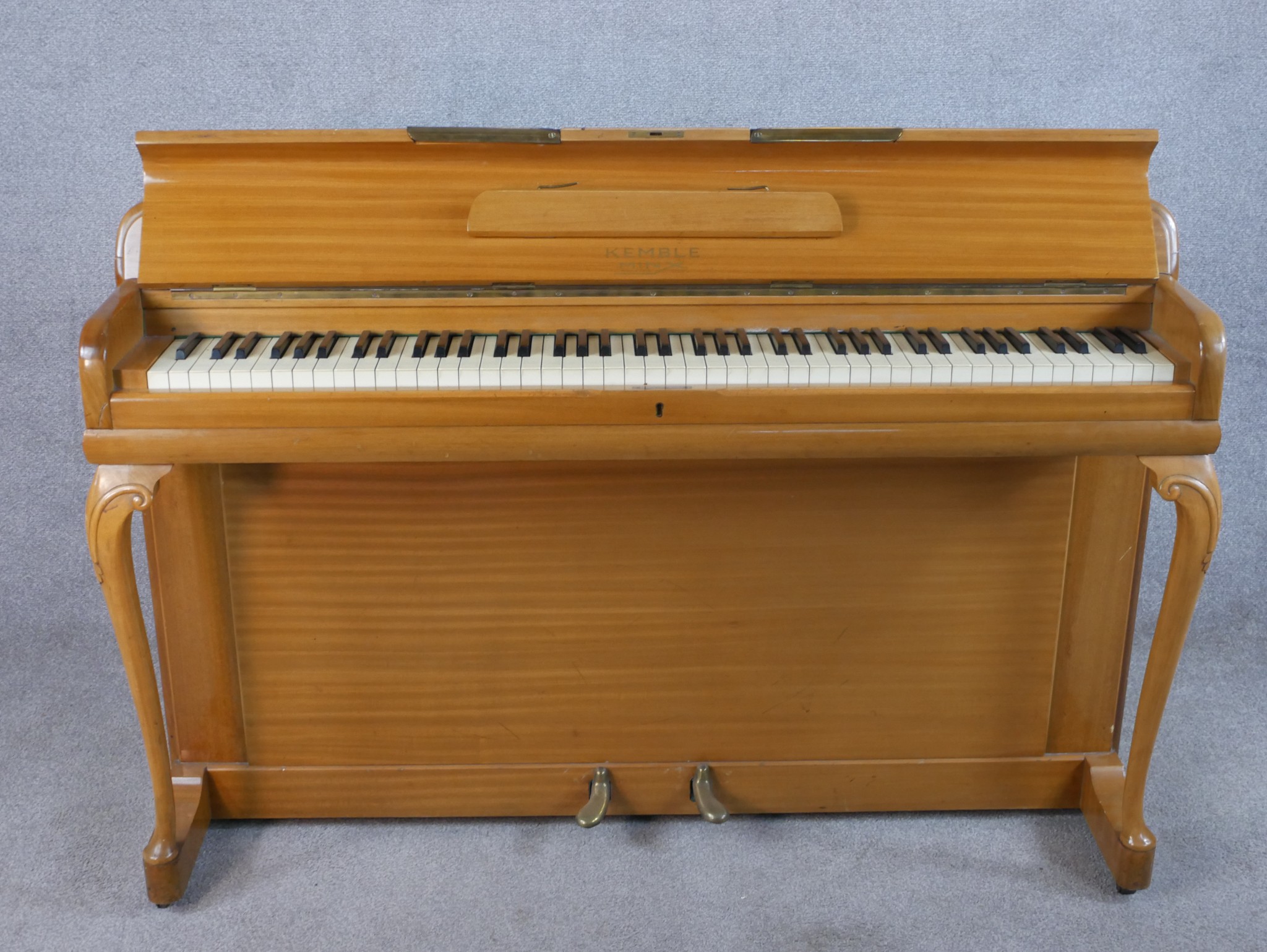 A mid 20th century Kemble beech upright piano raised on carved cabriole supports terminating on shap