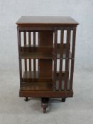 An early 20th century oak three shelf rotating book stand raised on metal cross shaped stretcher