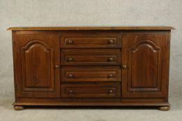 A contemporary oak sideboard with four central drawers flanked by two cupboard doors raised on squat