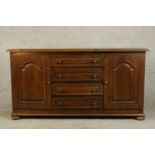 A contemporary oak sideboard with four central drawers flanked by two cupboard doors raised on squat