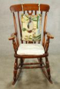 A 20th century mahogany Windsor style open arm splat back rocking chair raised on turned supports