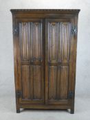 A 20th century stained oak twin door wardrobe with panels of linen fold decoration raised on