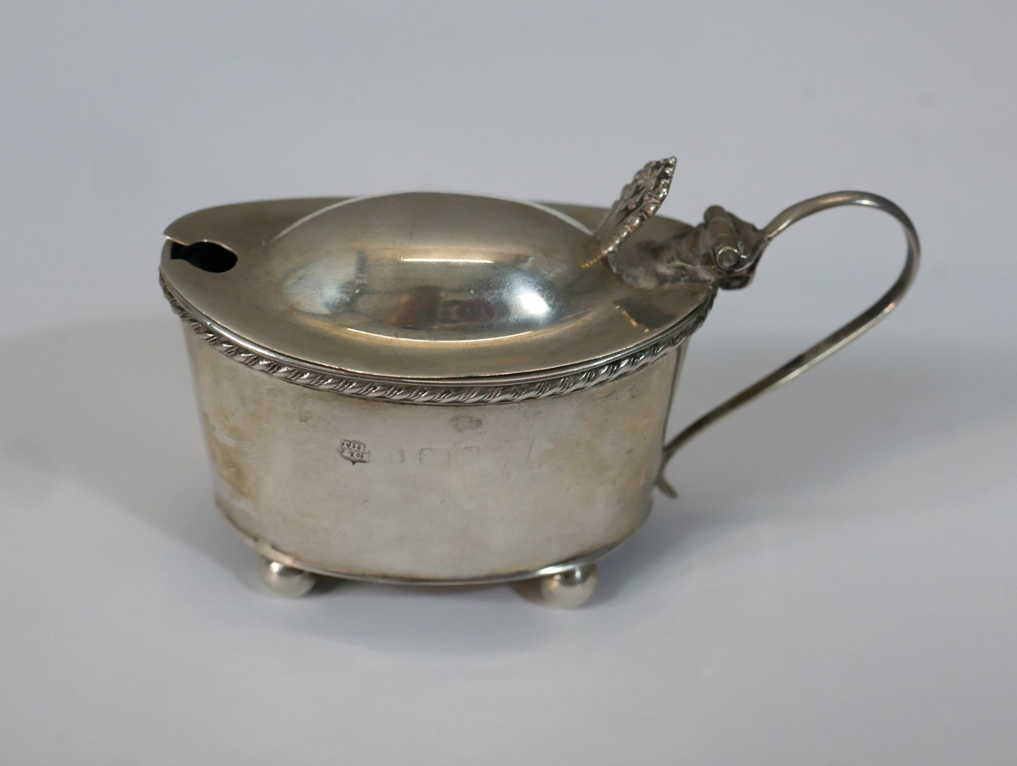 A 19th century hallmarked silver drum mustard (hallmarks worn) with 'S' scroll handle and cast thumb